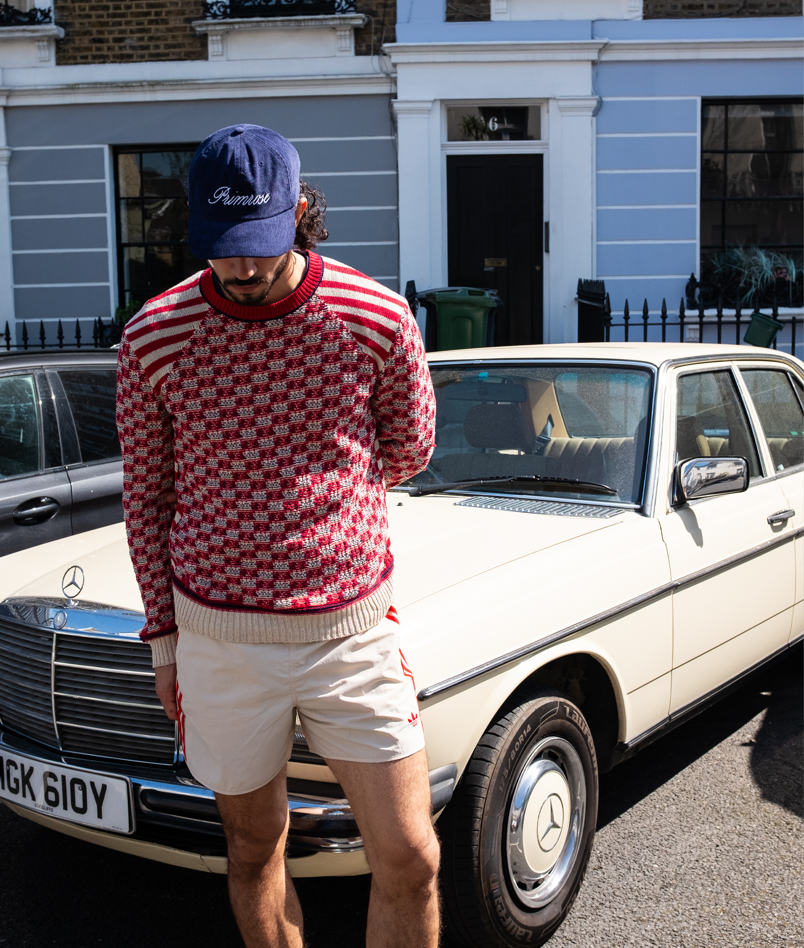 Person wearing a red checkered sweater and white shorts standing next to a vintage car.
