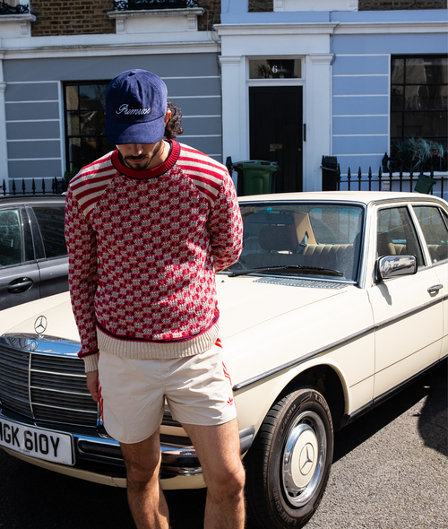 Person wearing a red checkered sweater and white shorts standing next to a vintage car.