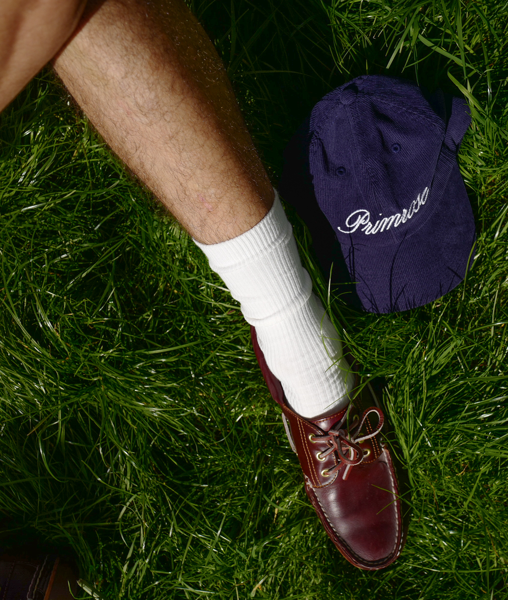 Person wearing a white sock and maroon shoe on grass with a blue cap labeled 'Primrose' in the background.