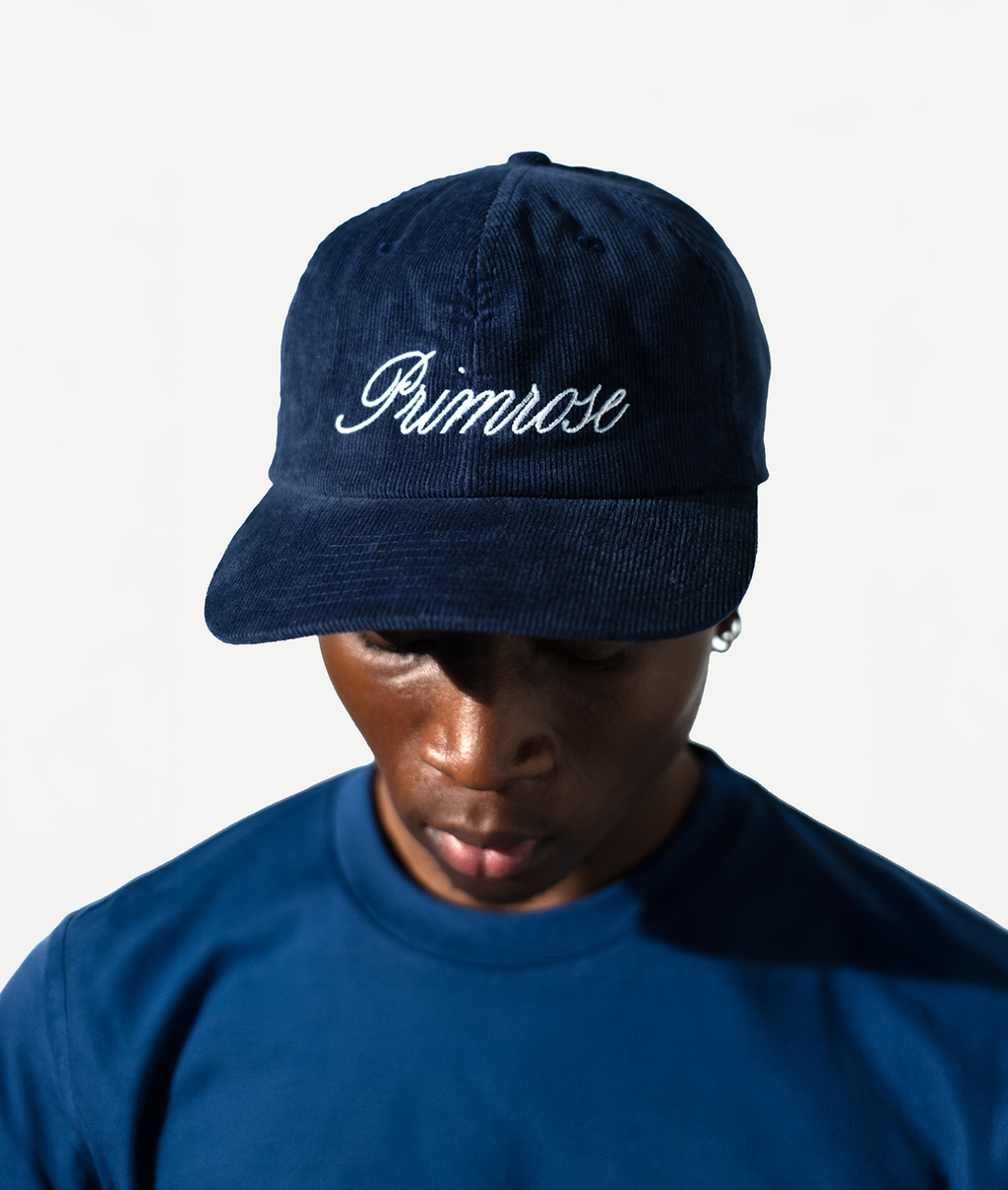 Person wearing a navy blue cap with 'Primrose' embroidered on it against a white background