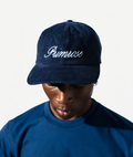 Person wearing a navy blue cap with 'Primrose' embroidered on it against a white background