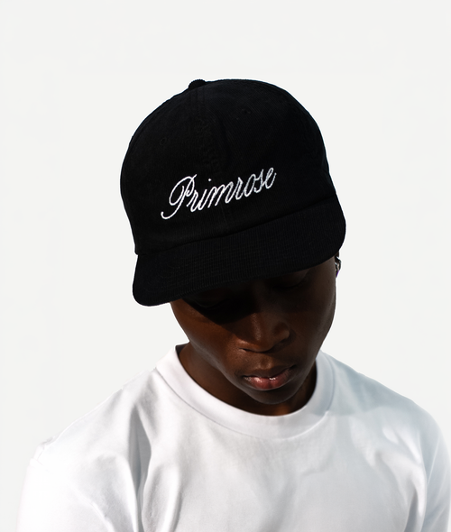 Person wearing a black cap with 'Primrose' embroidered on it against a white background