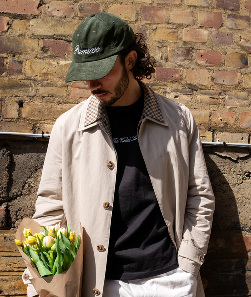 Man holding flowers against a brick wall, wearing Primrose London embroidered cap.