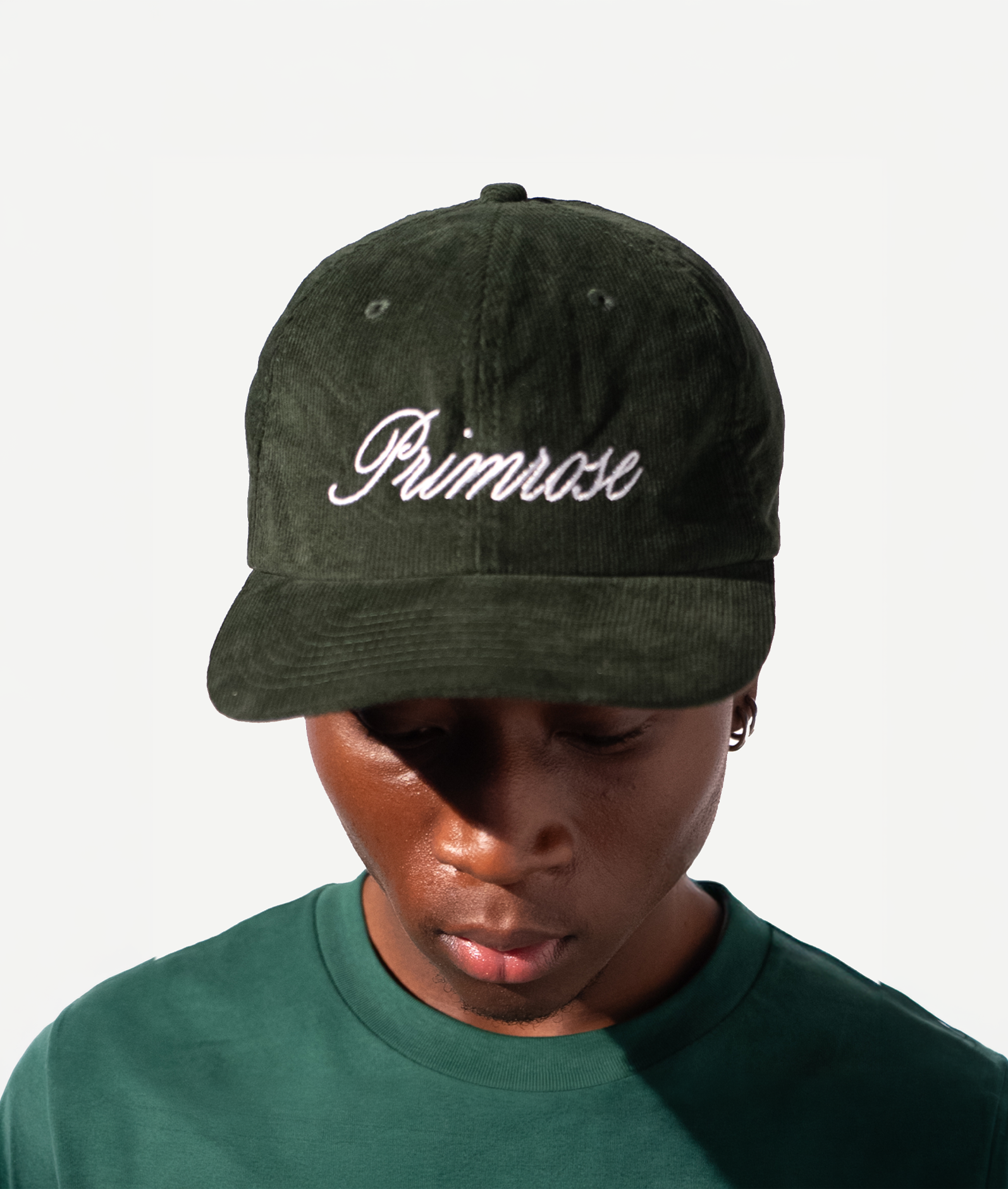 Person wearing a green cap with 'Primrose' embroidery on a white background
