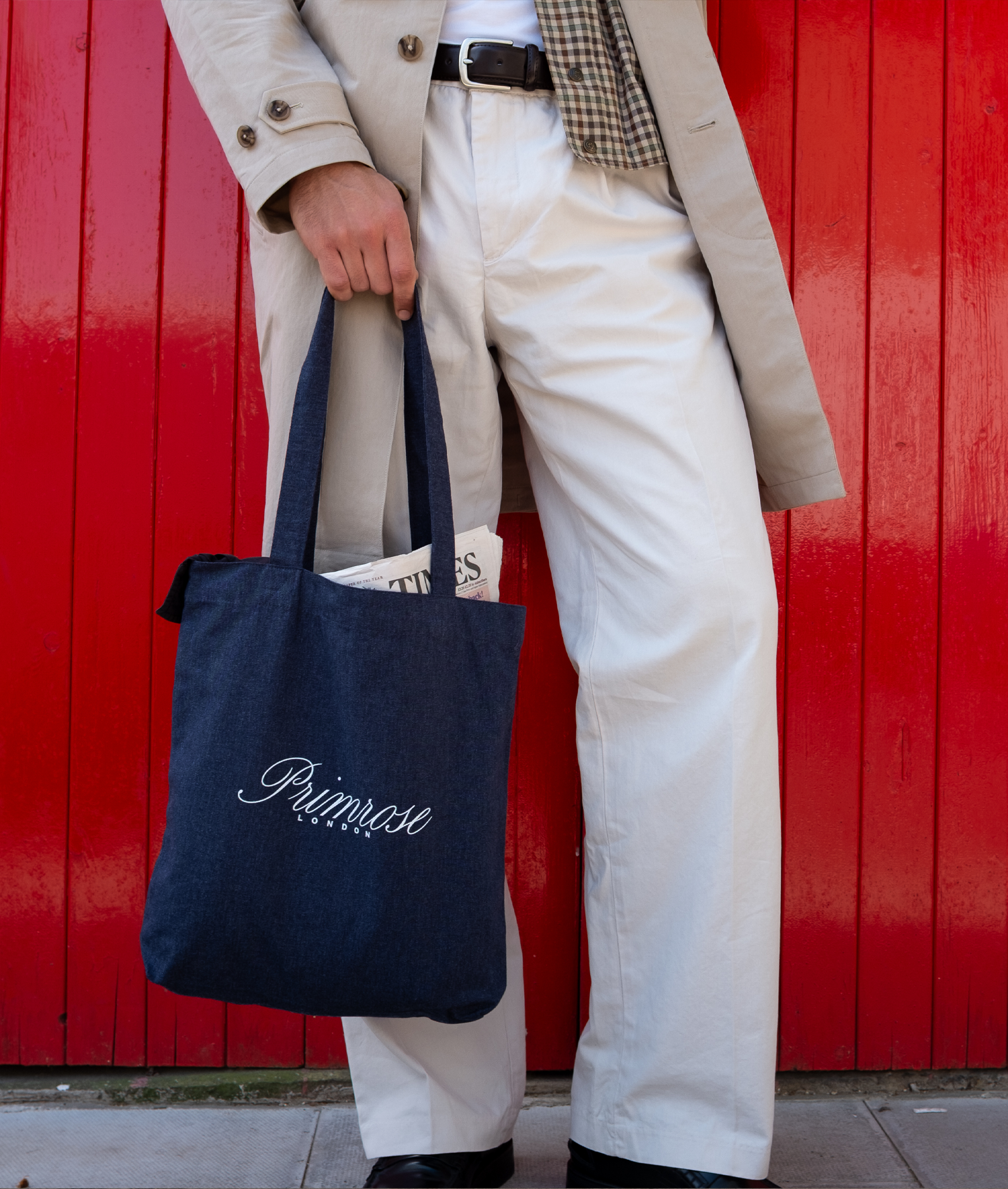 Person holding a navy tote bag with 'Primrose' branding against a red wall.