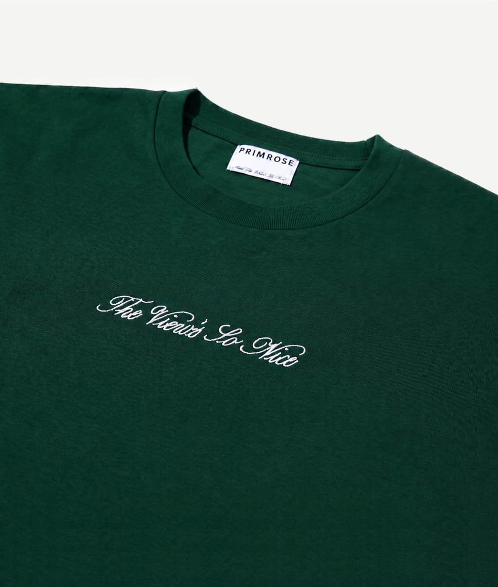 Green t-shirt with white text 'The View's So Nice' and 'Primrose' label on a light gray background