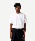 Person wearing a white t-shirt with text, black pants, and a black cap on a white background