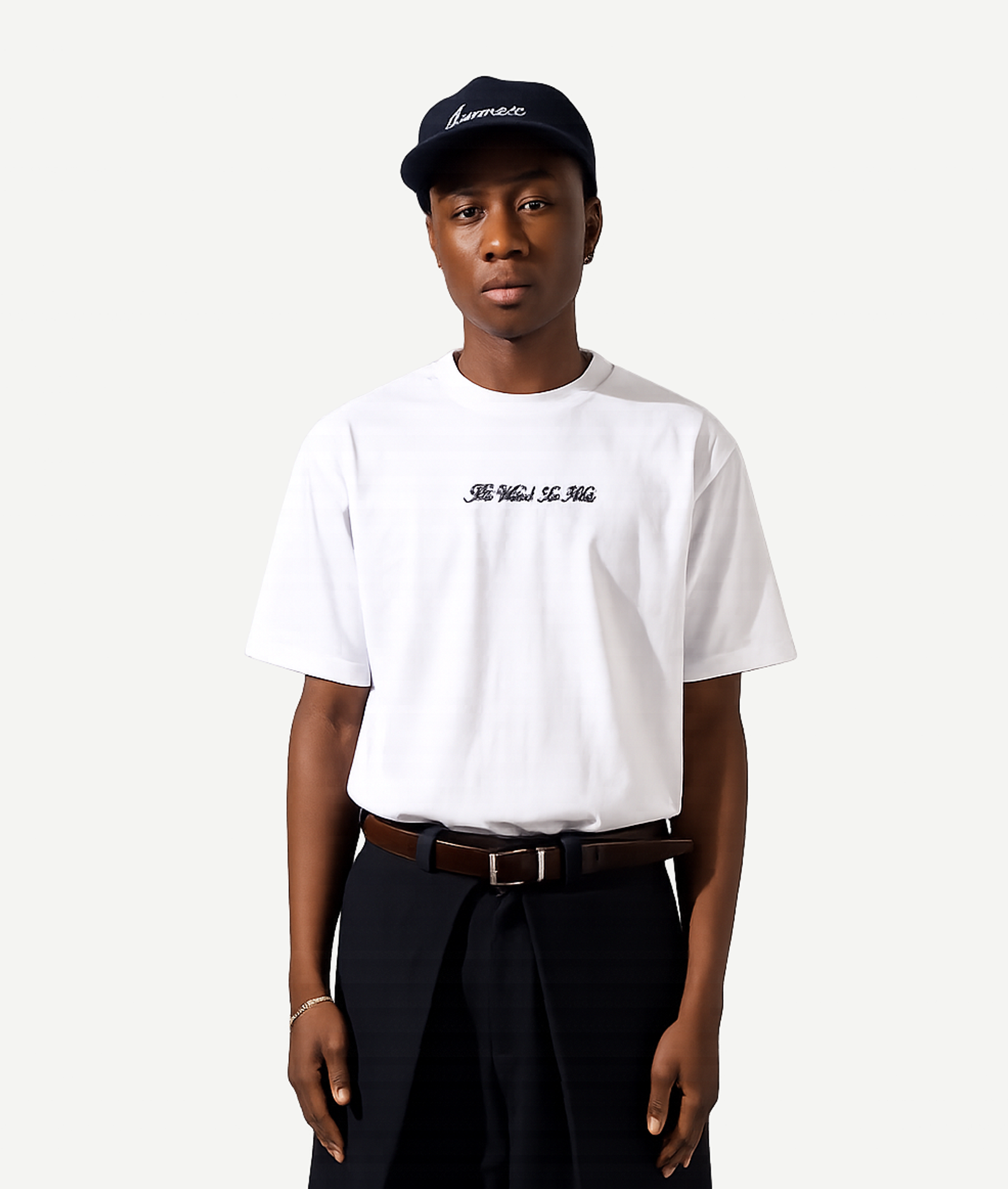 Person wearing a white t-shirt with text, black pants, and a black cap on a white background